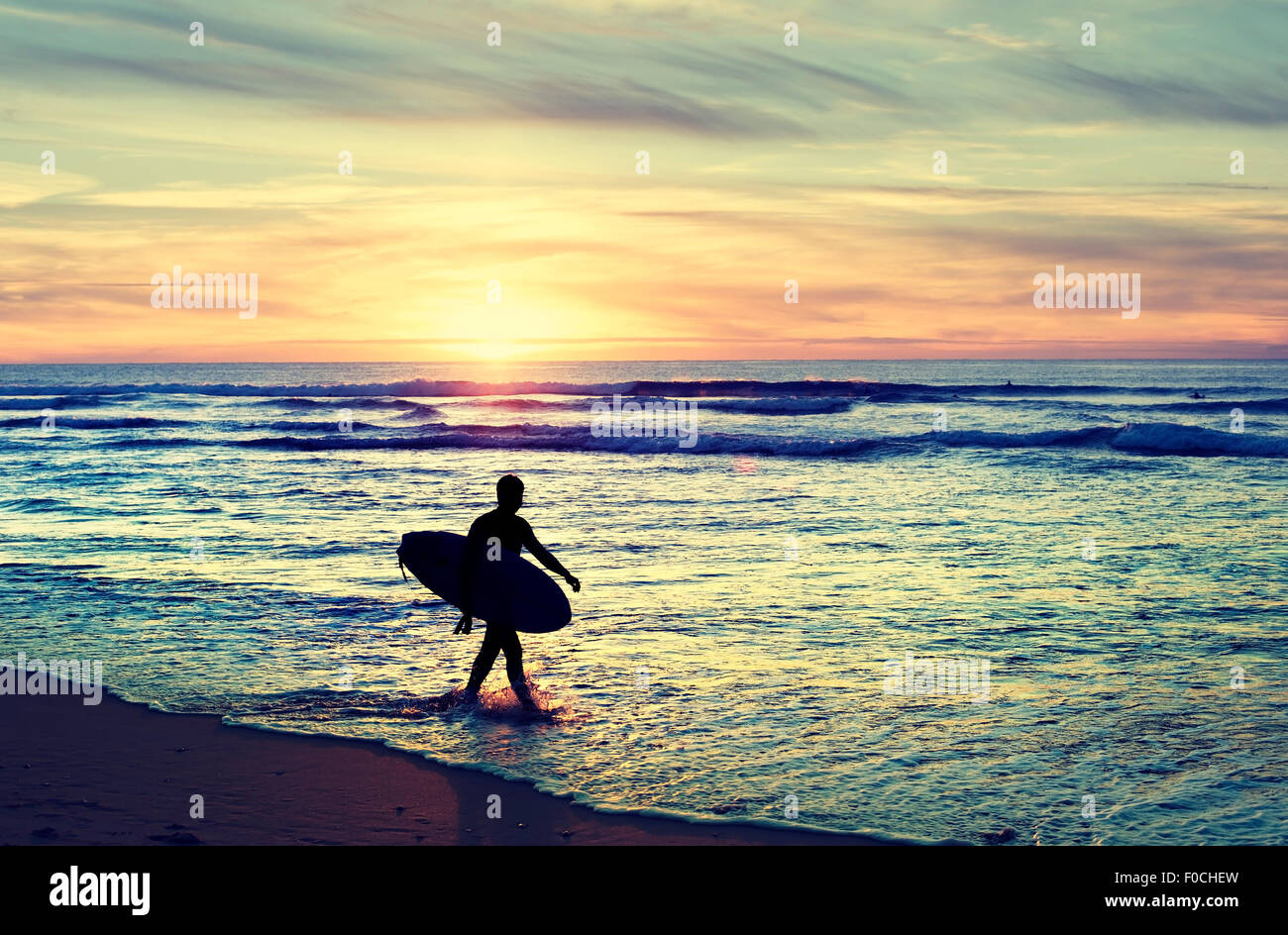 Surfer di camminare sulla spiaggia al tramonto. Colore vintage Foto Stock