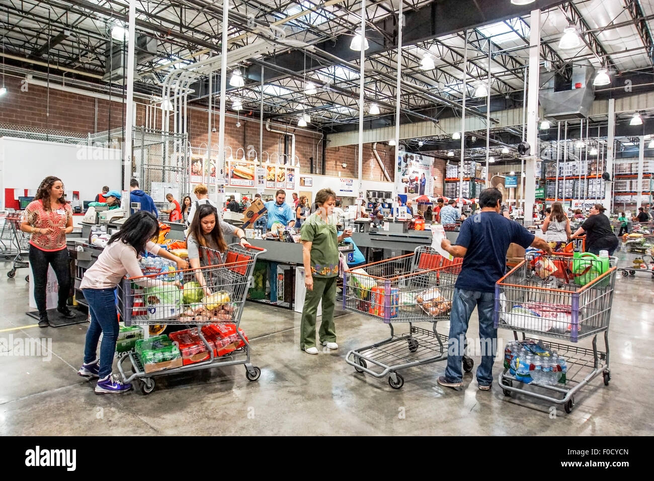 Asian giovane con 2 figlie adolescenti ridistribuire le merci nella loro 3 carrelli di shopping prima di entrare a far parte di controllo adiacente corsie fuori Costco Foto Stock