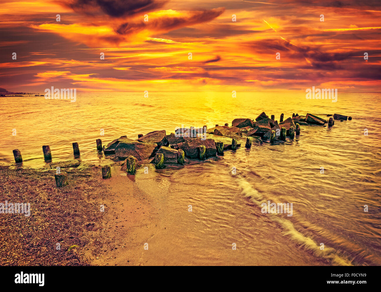 Vintage tonica drammatico tramonto sulla spiaggia e molo roccioso. Foto Stock