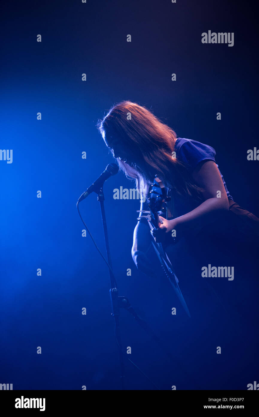 Giovane donna, 20-24, cantante chitarrista effettuando in corrispondenza di un concerto dal vivo a New York con evidenziazione blu illuminazione scenica Foto Stock