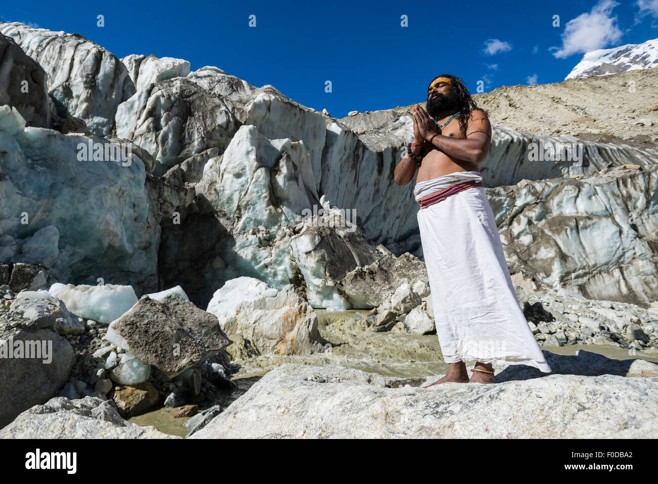 Un Sadhu, uomo santo, è in piedi e pregando su una roccia a Gaumukh, la fonte principale di fiume santo Ganges, Gangotri, Uttarakhand Foto Stock