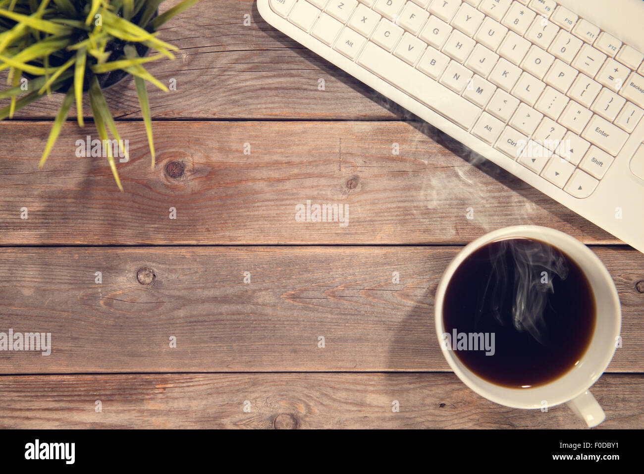 Vista superiore dello spazio di lavoro con la tastiera del computer, una tazza di caffè e impianto pot. Tavolo in legno sfondo nel vintage tonica. Foto Stock