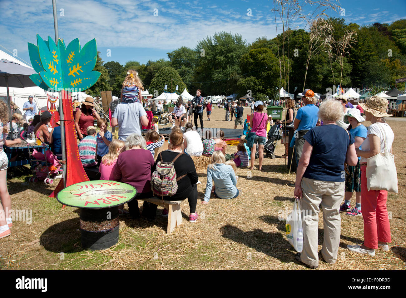 Famiglie guarda animatori nel sole estivo da stand gastronomici e tabelloni elettronici al porto Eliot Festival Cornovaglia Foto Stock