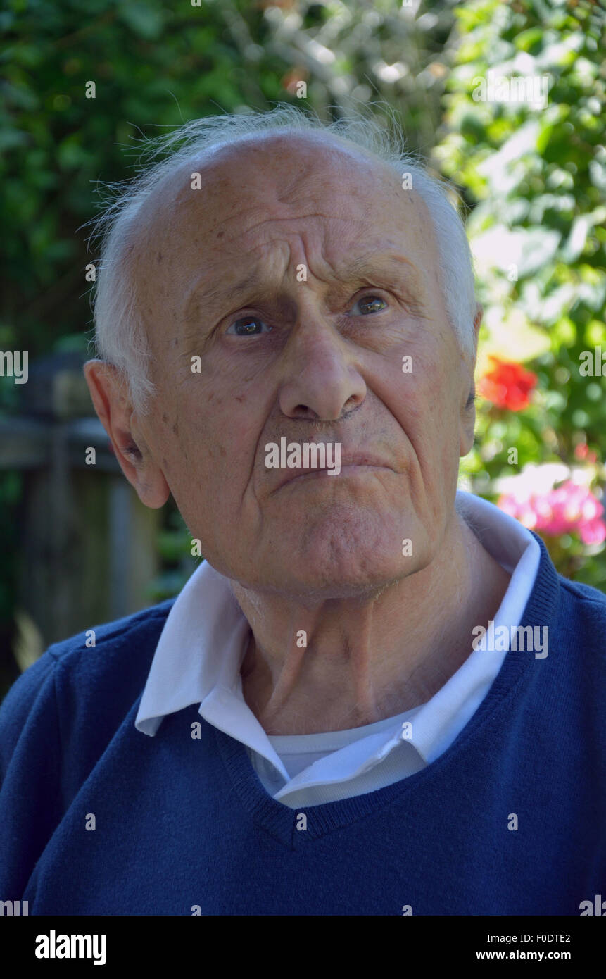 Un uomo anziano che soffrono di demenza seduta tranquillamente cercando perso nei suoi pensieri. Foto Stock