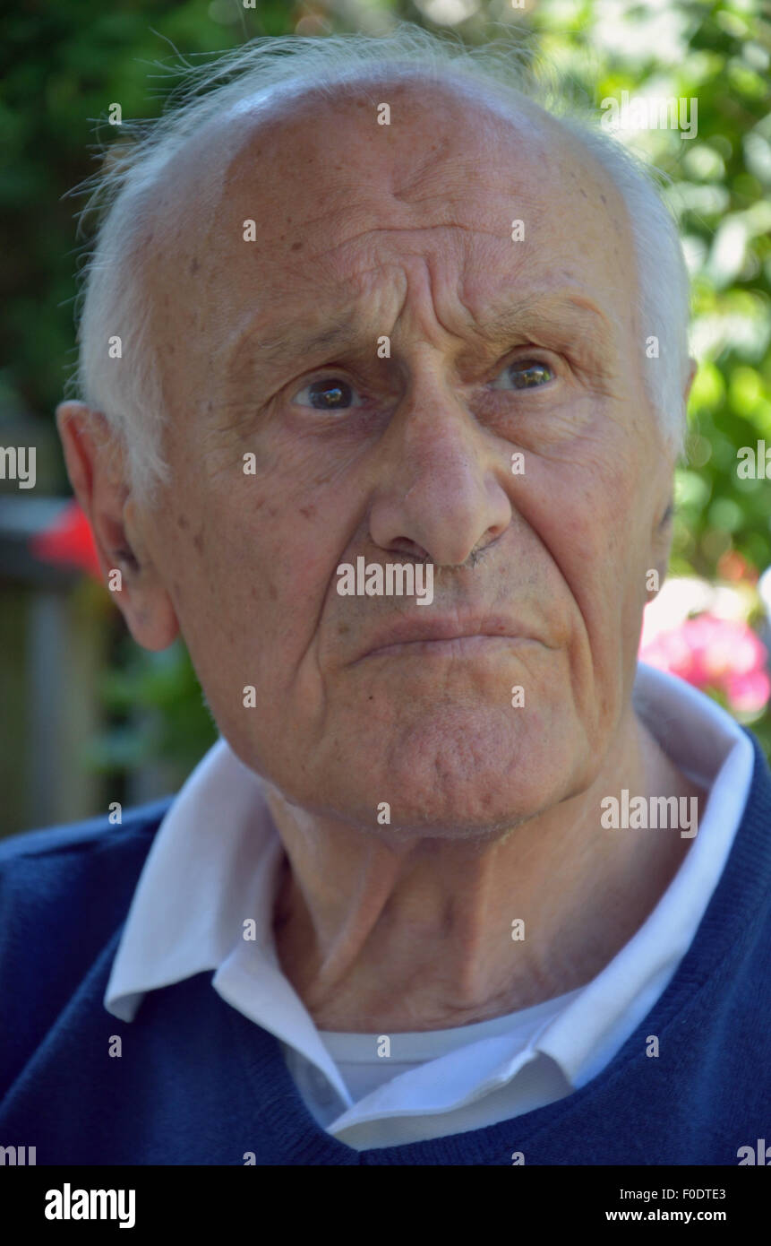 Un uomo anziano che soffrono di demenza seduta tranquillamente cercando perso nei suoi pensieri. Foto Stock