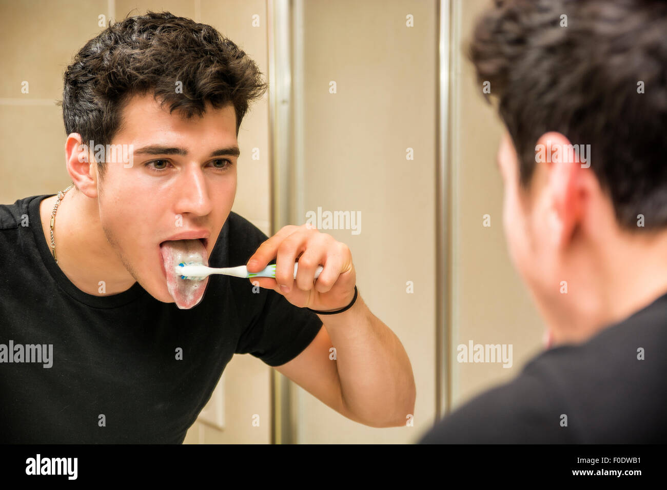 Colpo di Testa di attraente giovane di spazzolare i denti e la lingua per la pulizia con spazzolino da denti, guardando a se stesso in specchio Foto Stock