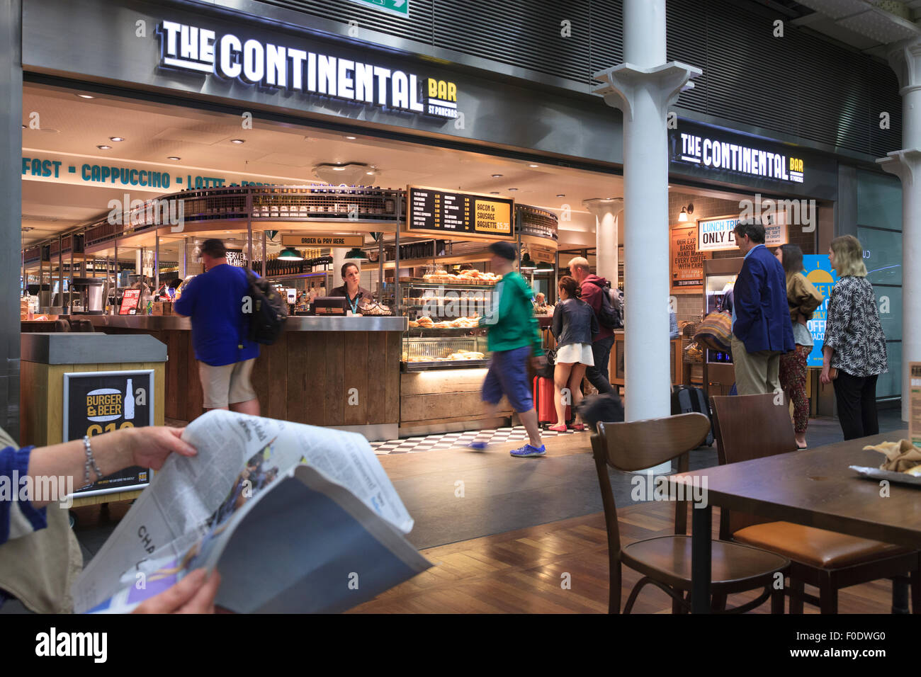 Un cliente legge un giornale mentre altri la coda per la prima colazione presso il terminal Eurostar St Pancras Londra Foto Stock
