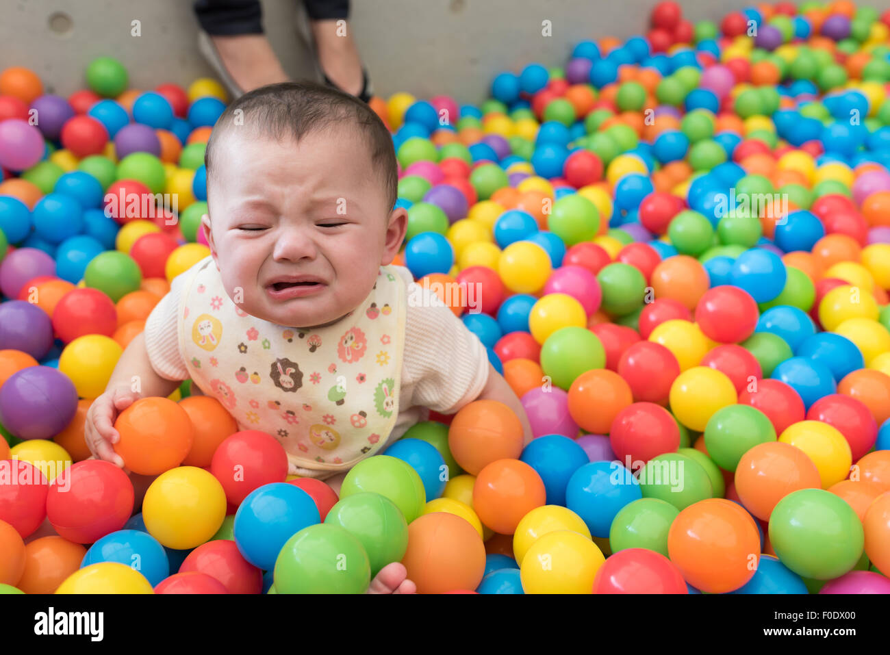 Una bella ragazza che piange seduto in una sfera colorata buca ad un parco giochi. Foto Stock