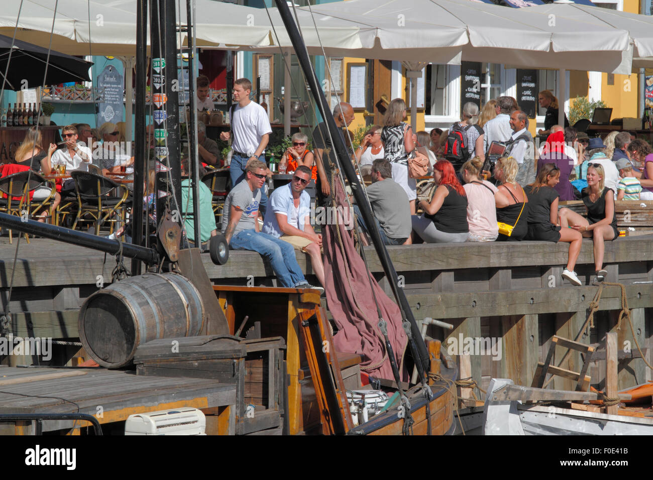 Le persone a incontrarsi e discutere su un drink al sole sulla banchina in ambiente accogliente in un affascinante Nyhavn. Molti preferiscono sedere sul pontile tra le vecchie navi. Hygge. Foto Stock
