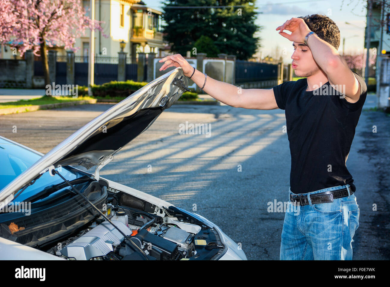 Bel giovane cercando di riparare il motore di una macchina, guardando all'interno di aprire il cofano Foto Stock