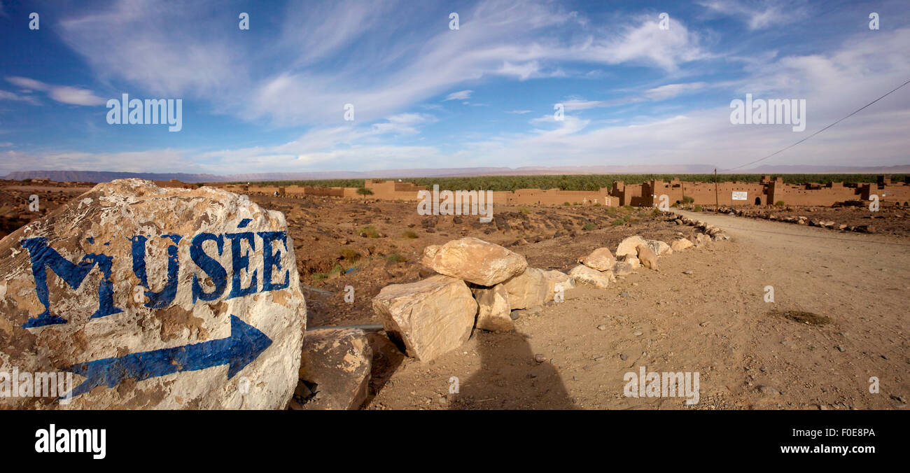 Freccia blu e museo dipinta su una pietra in un piccolo villaggio nel deserto del sud del Marocco. Foto Stock