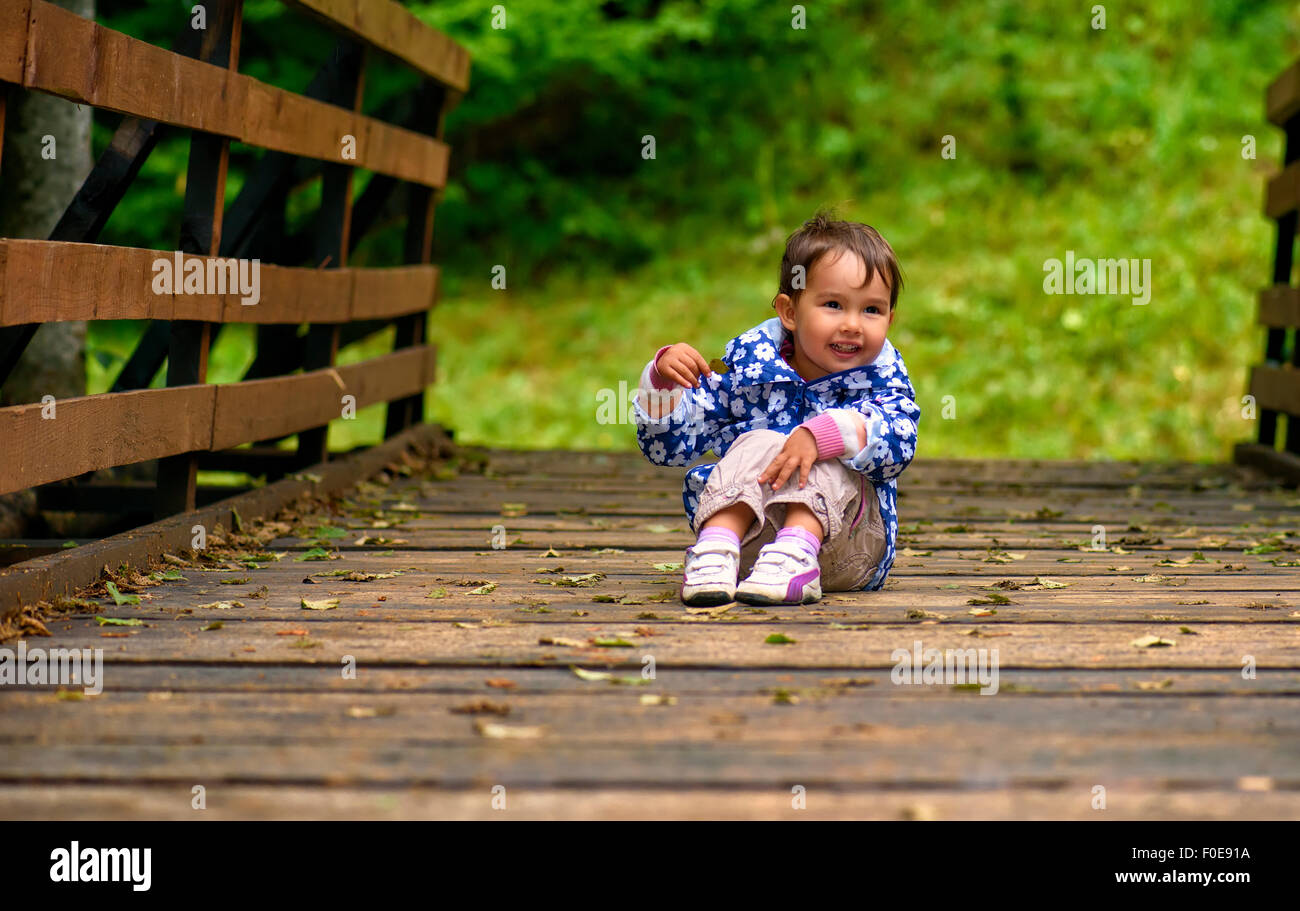 Poco ragazza seduta sul ponte al giorno Foto Stock