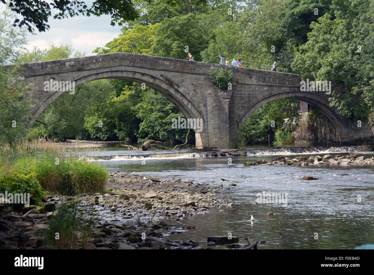 Walkers attraversare il Ponte Vecchio, Ilkley Yorkshire, che è costruita di pietra attraversa il fiume Wharfe a Ilkley Yorkshire Inghilterra Foto Stock