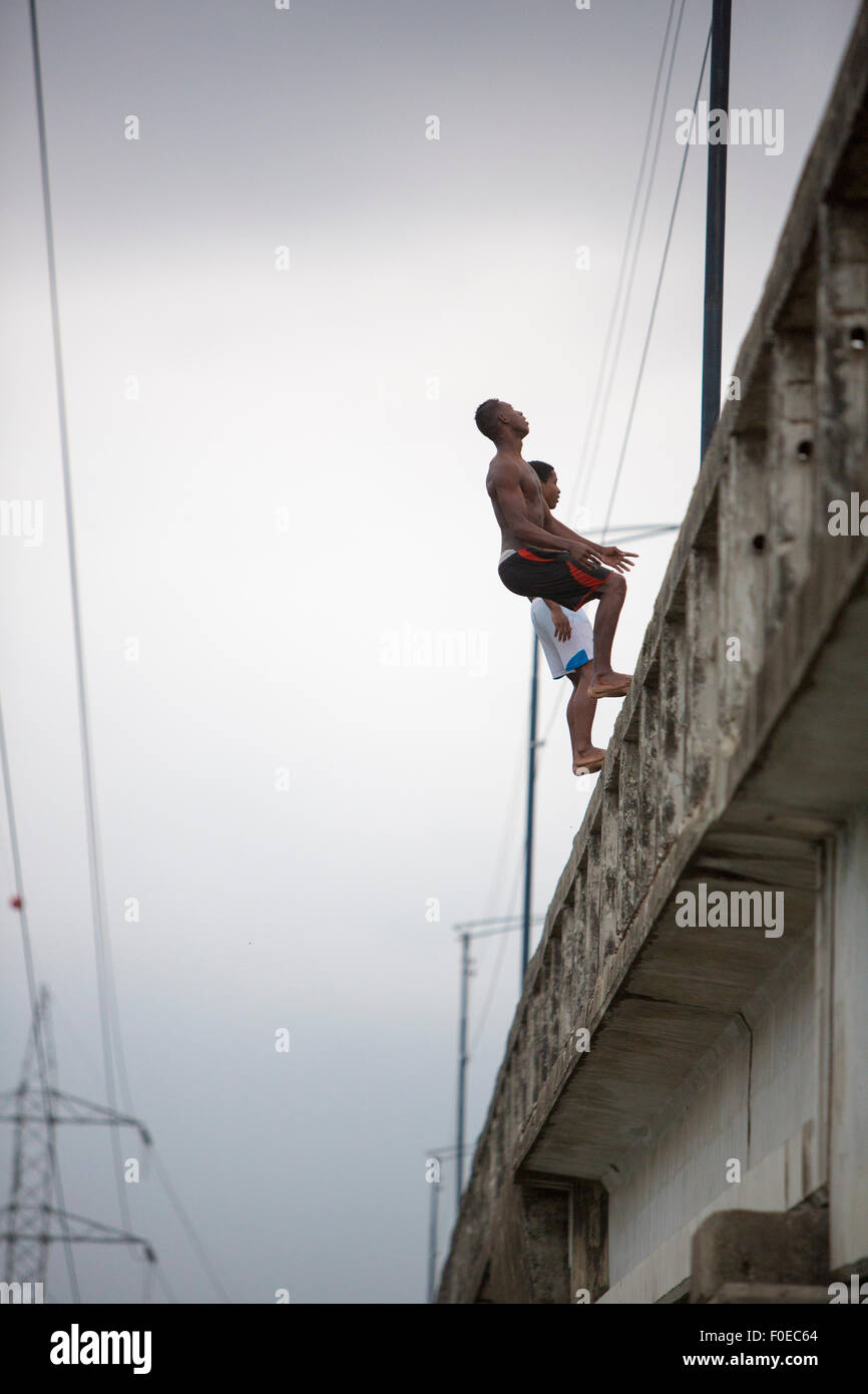 Due adolescenti non identificato jumping lato posteriore da un alto ponte concreto al fiume nella città di Guayaquil. Ecuador 2015. Foto Stock