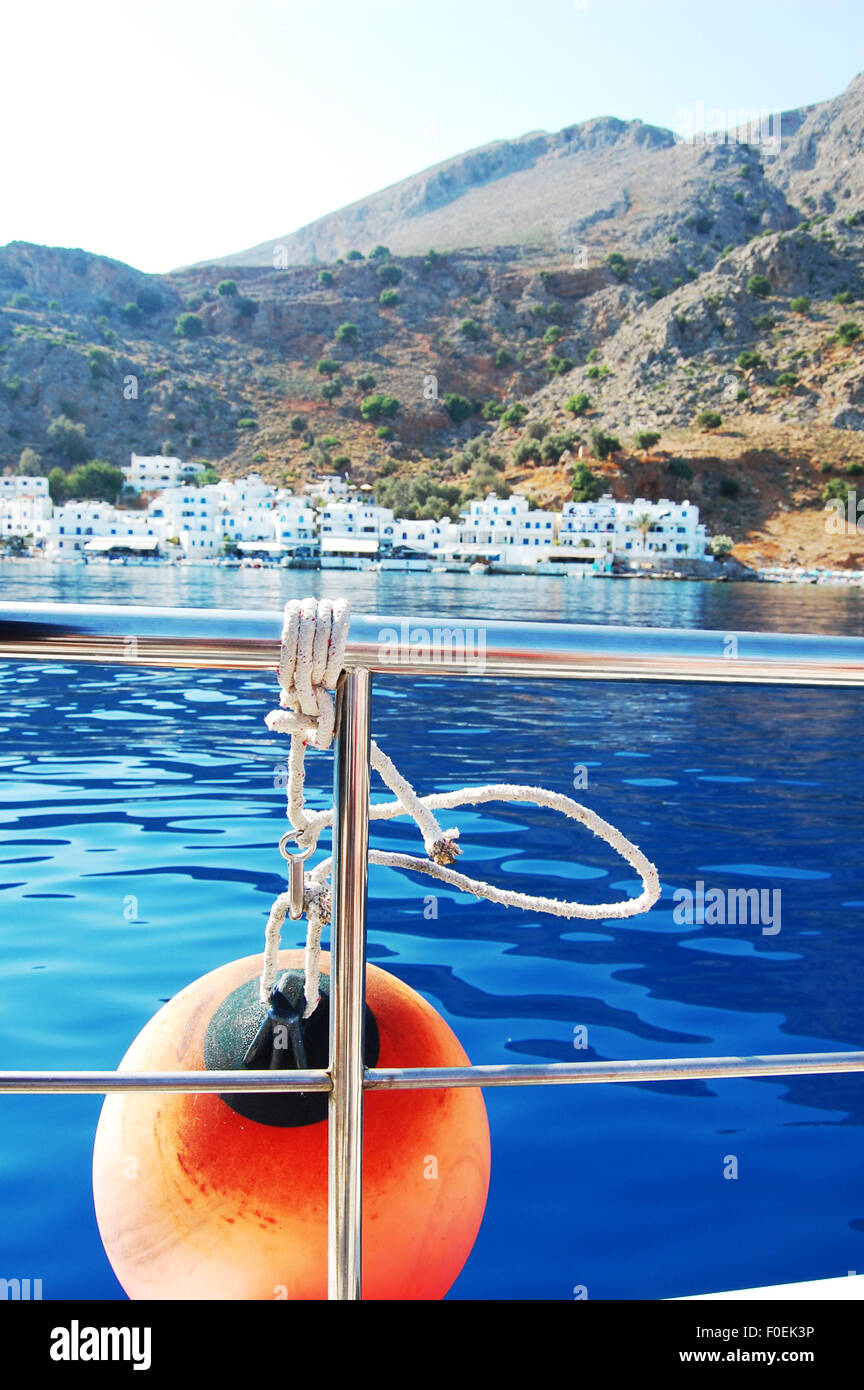 Galleggiante arancione sul lato di una barca in Creta Grecia con il villaggio di Loutro in background Foto Stock