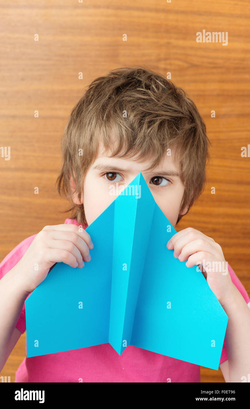 Un giovane bambino azienda blue aeroplano di carta nella parte anteriore del viso Foto Stock