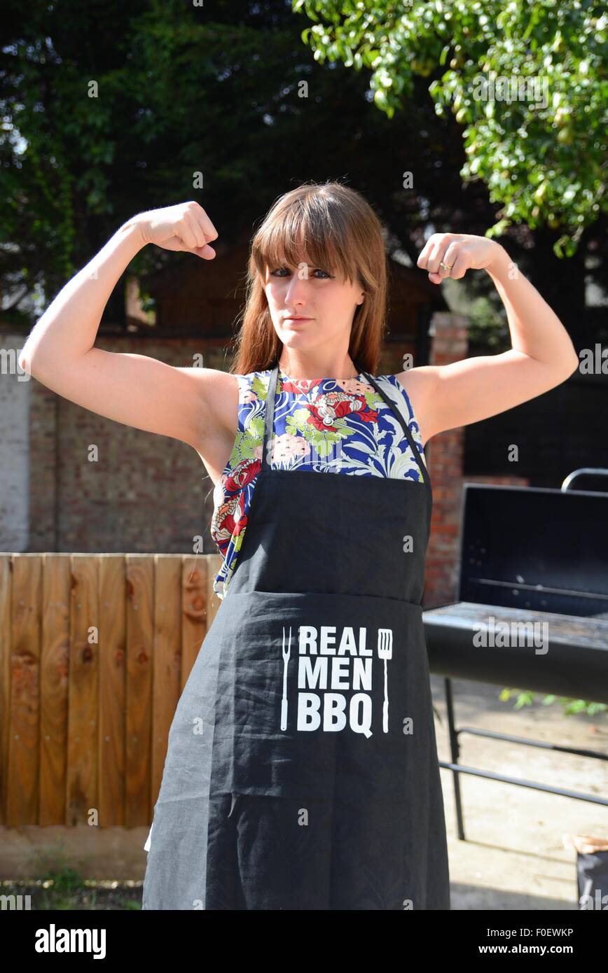 Attraente giovane donna che mostra la forza femminile di indossare un grembiule barbecue all'aperto Foto Stock