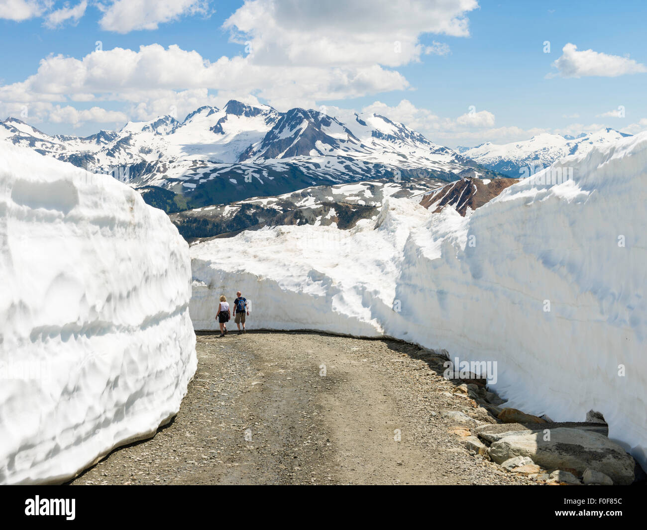 Due escursionisti sulla Mathew traversa della strada tagliata attraverso il "muro di ghiaccio' di neve, Whistler Mountain, BC, Canada. Foto Stock