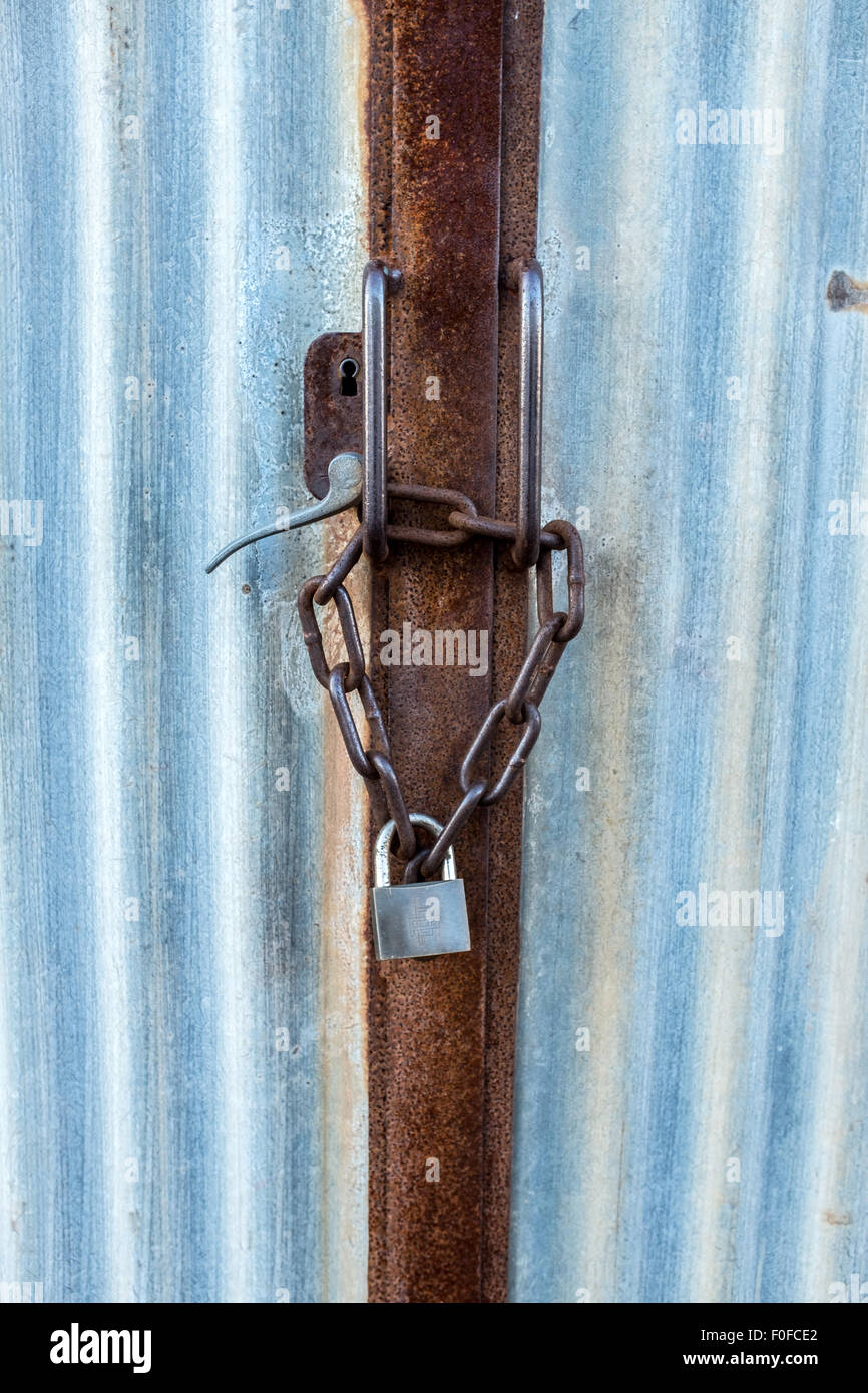 Rusty catena e un lucchetto su un ferro corrugato porta Foto Stock
