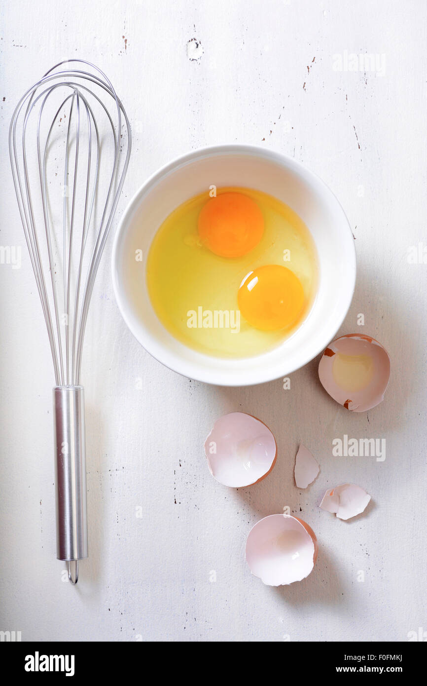 Concetto di cucina a vista con le uova rotte e frusta di metallo su vintage Sfondo legno. Foto Stock