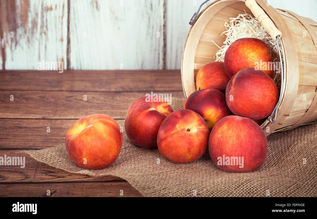 Pesche fresche di frutta in una cesta, rustico sfondo di legno Foto Stock