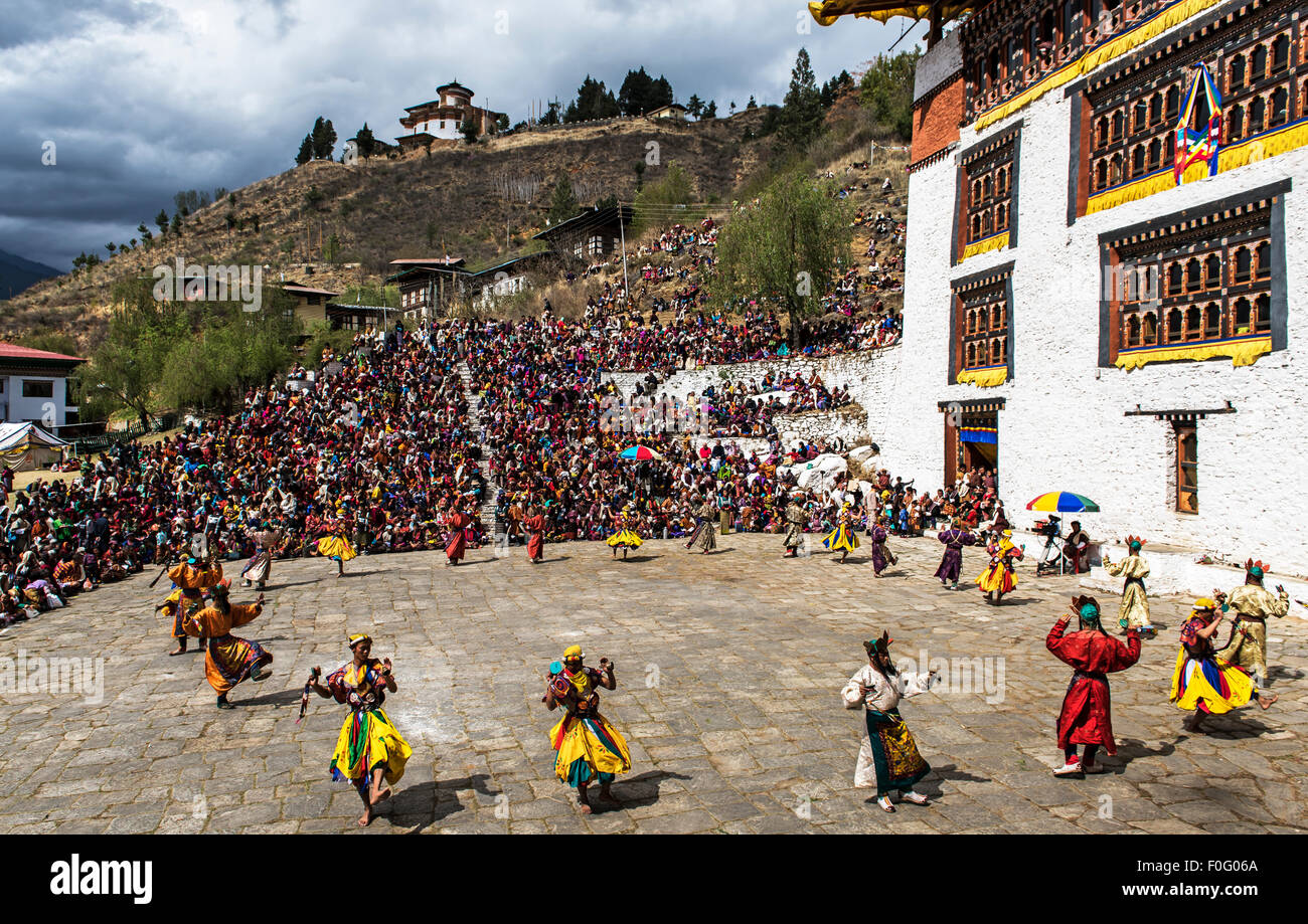 Ballerini di eseguire con gli spettatori e il tempio in background di Paro festival religioso del Bhutan Foto Stock