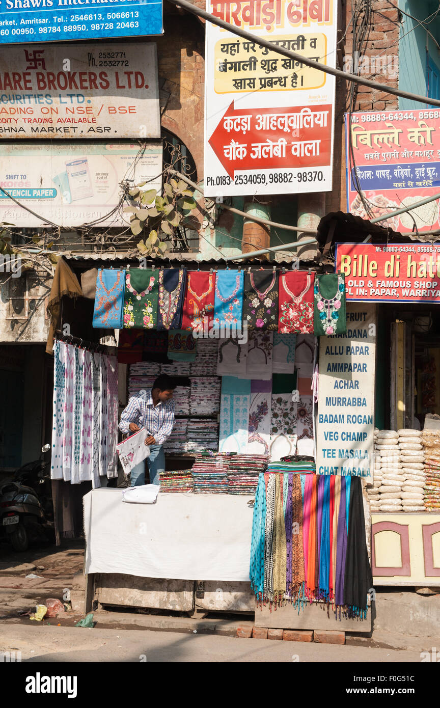 Amritsar Punjab, India. Scena di strada; colorato di stallo stradale la vendita delle t-shirt, tovaglie e altri tessuti con una ridda di segni sopra in western e Hindi script. Foto Stock