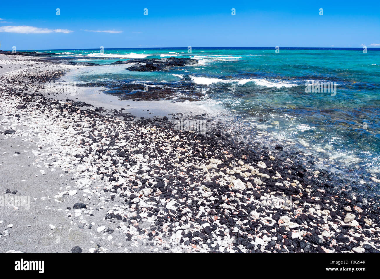 Un bel bianco e nero spiaggia di ghiaia con chiare acque blu su una spiaggia remota in Kona Hawaii. Foto Stock