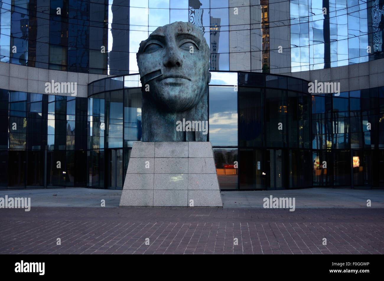 Una statua in bronzo del capo di un uomo circondato da un moderno, vetro edificio per uffici. Foto Stock