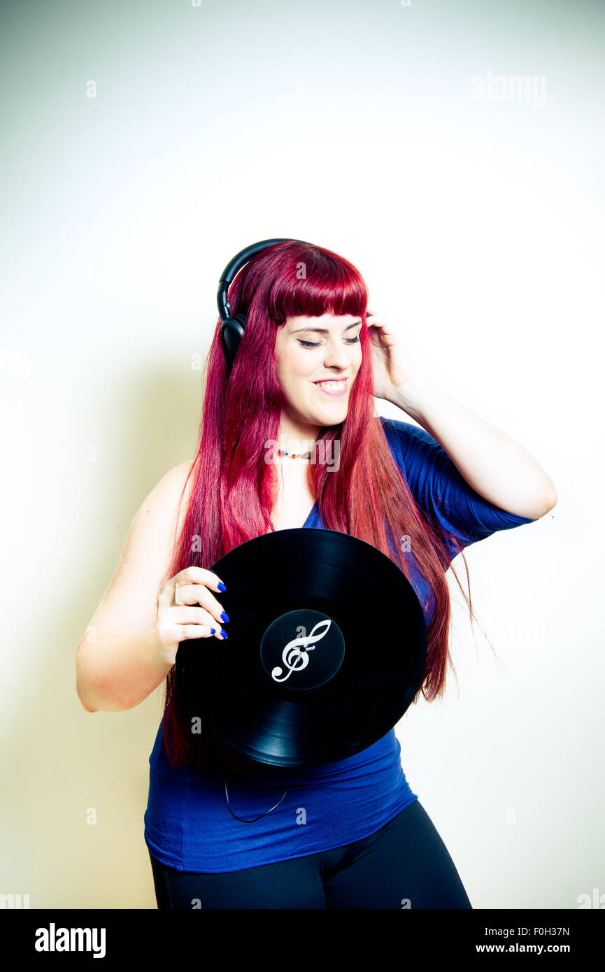 Giovane donna graziosa ballando con le cuffie e dischi in vinile con chiave di violino simbolo telaio verticale Foto Stock
