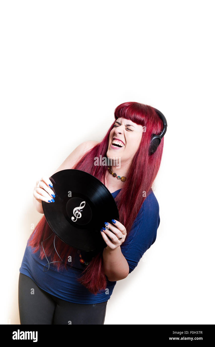 Giovane donna graziosa ballando con le cuffie e dischi in vinile con chiave di violino simbolo telaio verticale Foto Stock