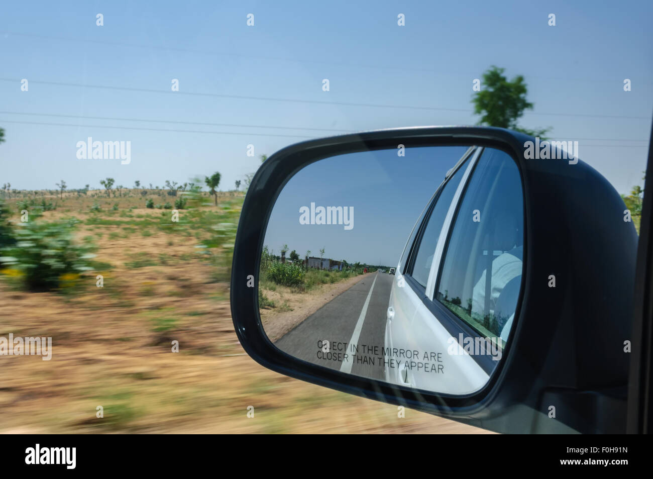 Vista attraverso lo specchietto retrovisore di una vettura in movimento su autostrada attraverso il deserto in alta velocità con moto circostante sfocata spazio di copia Foto Stock