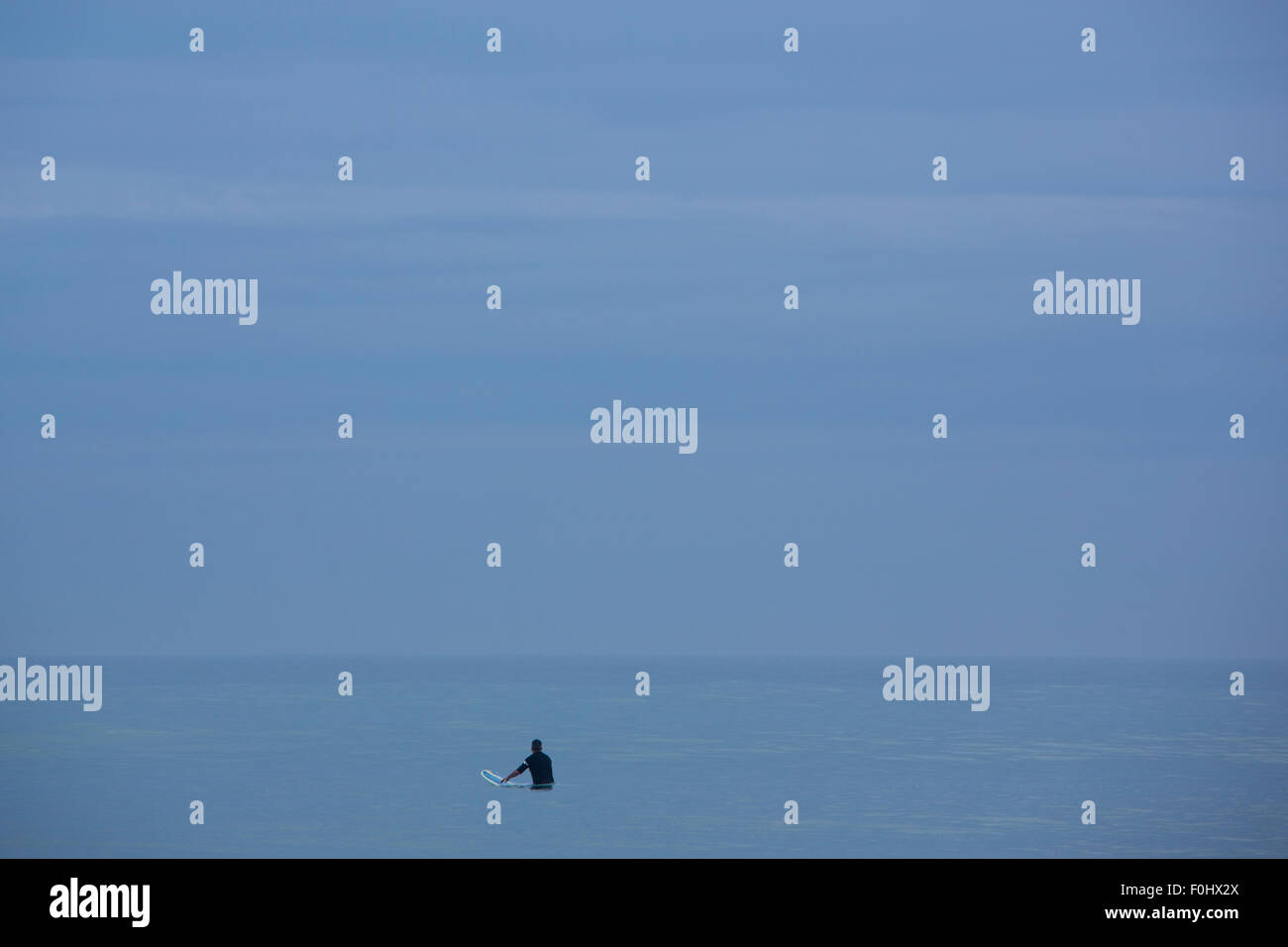 Blue Horizon piatta con un surfer in attesa con una scheda di navigazione l'onda perfetta nelle prime ore del mattino, Mancora. Perù Foto Stock