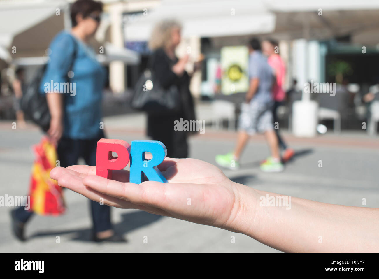 Le donne in attesa di lettere in legno PR. La gente a piedi sullo sfondo Foto Stock