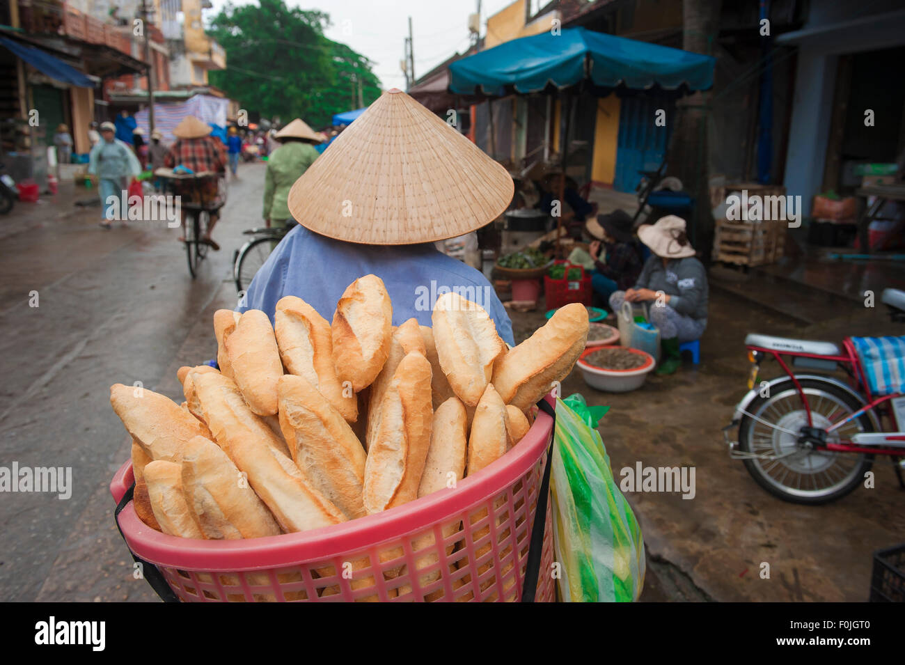 Cappello donna Vietnam, vista posteriore di una donna che indossa un cappello conico che trasporta pane al mercato di Hoi An, Vietnam centrale. Foto Stock
