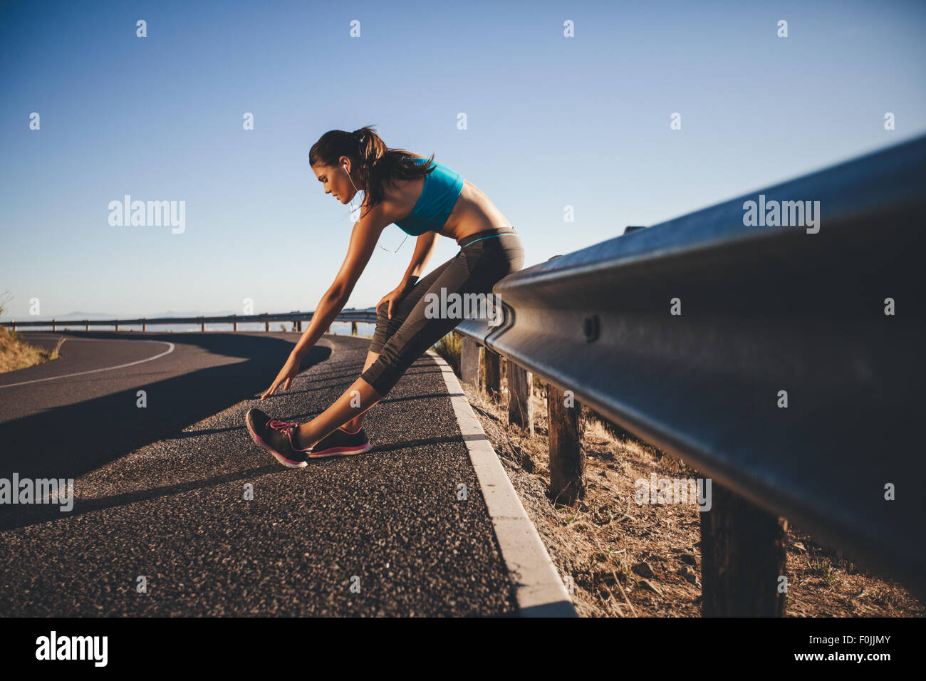 Giovane donna facendo stretching dopo una corsa. Runner appoggiata sul guardrail stradali la sua distensione dei muscoli del polpaccio. Foto Stock