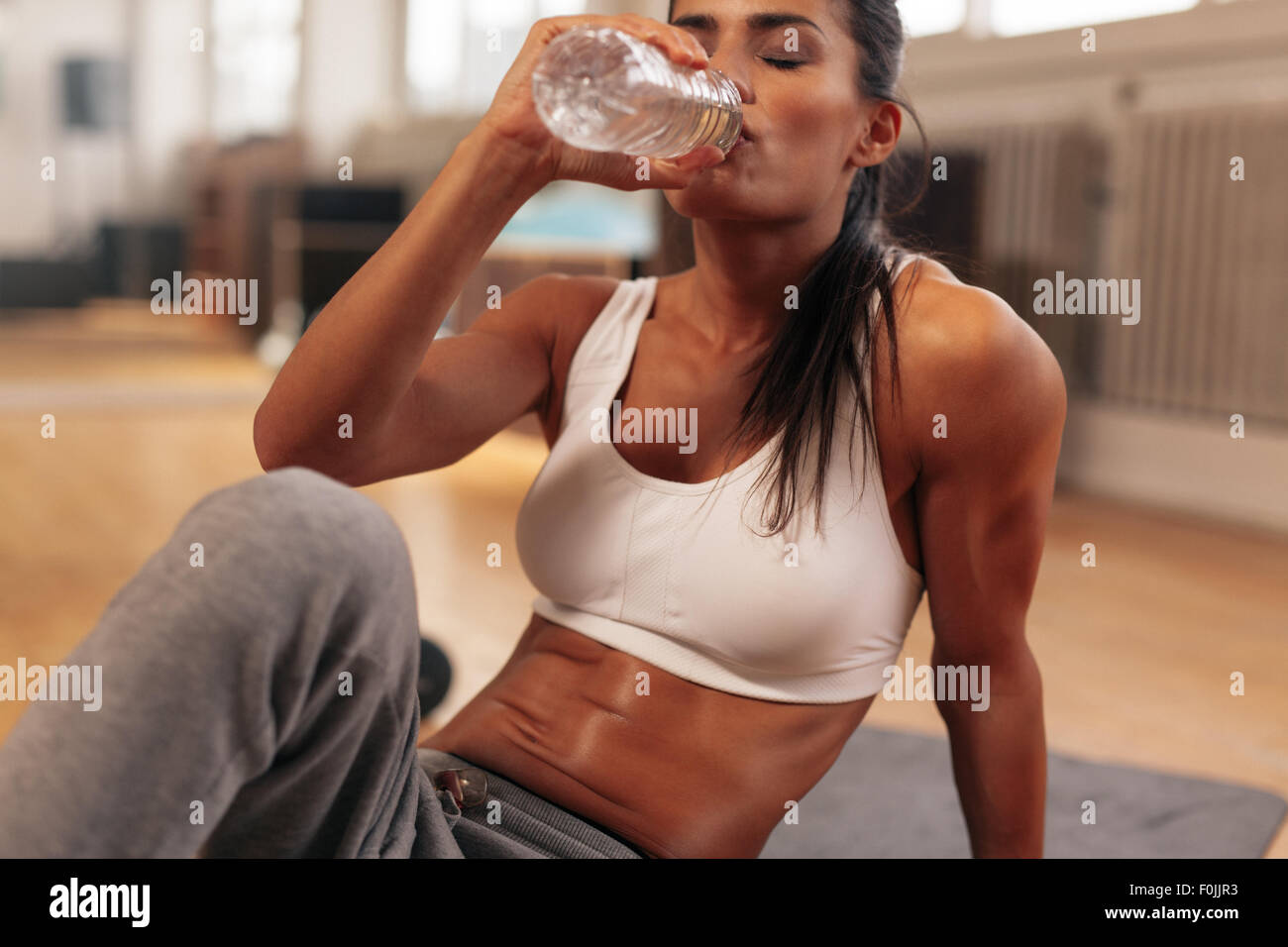 Donna Fitness acqua potabile dalla bottiglia. Muscolare di giovani donne presso la palestra prendendo una pausa da allenamento. Foto Stock