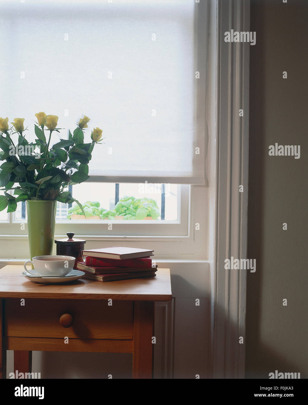 Tessuto bianco di tenda a rullo con un tavolo e un vaso di rose giallo, tazza e piattino e fiore premere nella parte anteriore di essa. Foto Stock