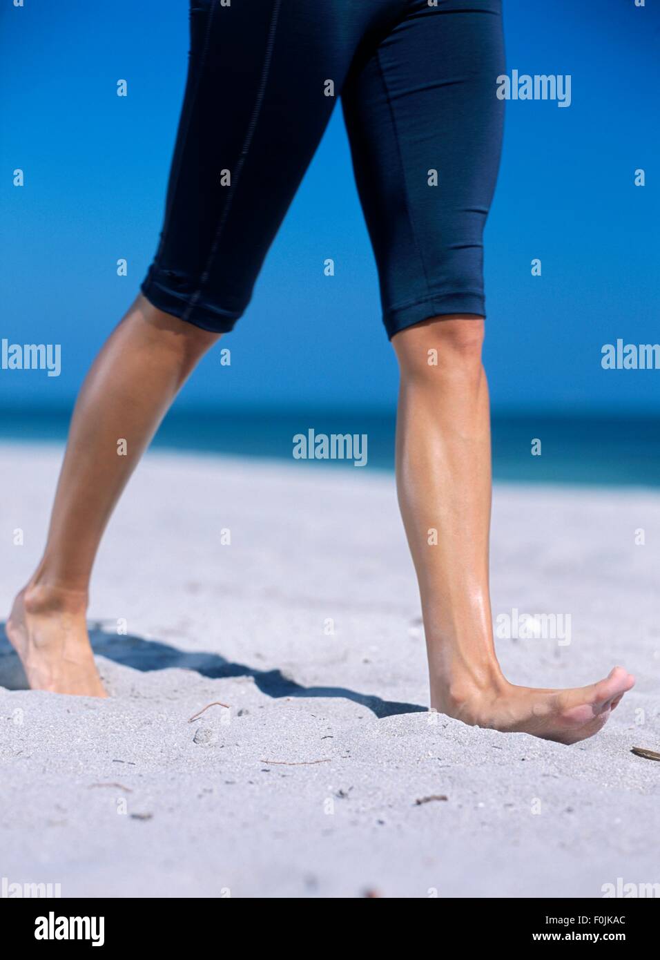 Donna che indossa gambali breve camminare a piedi scalzi nella sabbia, close-up sulle gambe Foto Stock