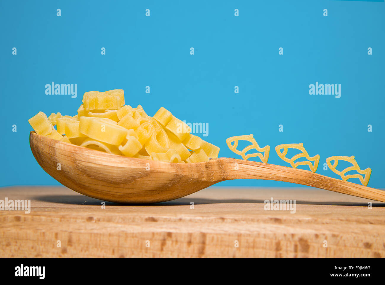 La pasta in forma di animali e un cucchiaio di legno su uno sfondo blu Foto Stock