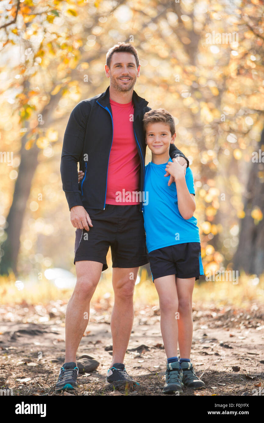 Ritratto sorridente padre e figlio nell'abbigliamento sportivo sul percorso nel bosco Foto Stock