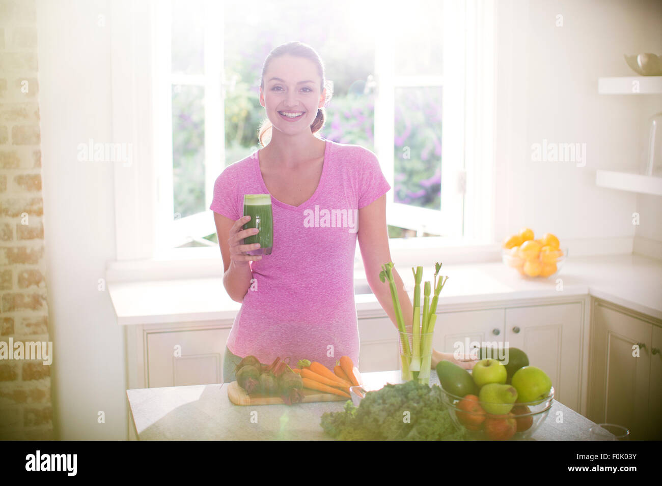 Ritratto di donna sorridente bere frullato verde in cucina Foto Stock