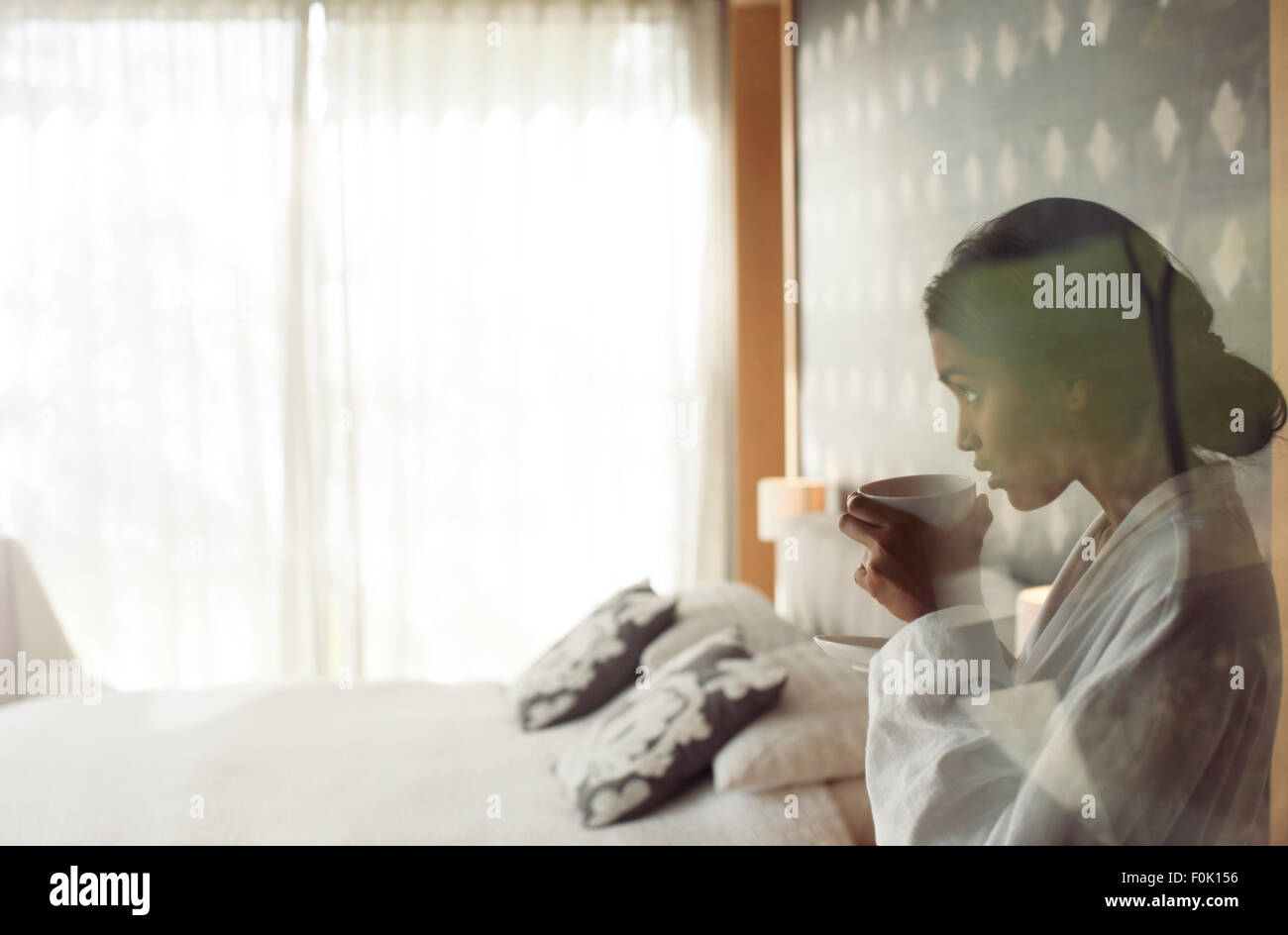 Donna in accappatoio sorseggiando caffè in camera da letto Foto Stock