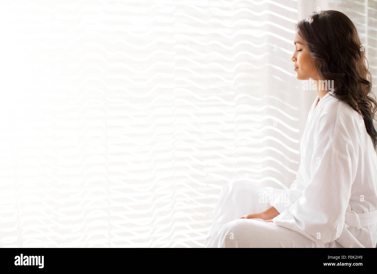 Serena donna in accappatoio meditando a finestra piena di sole Foto Stock
