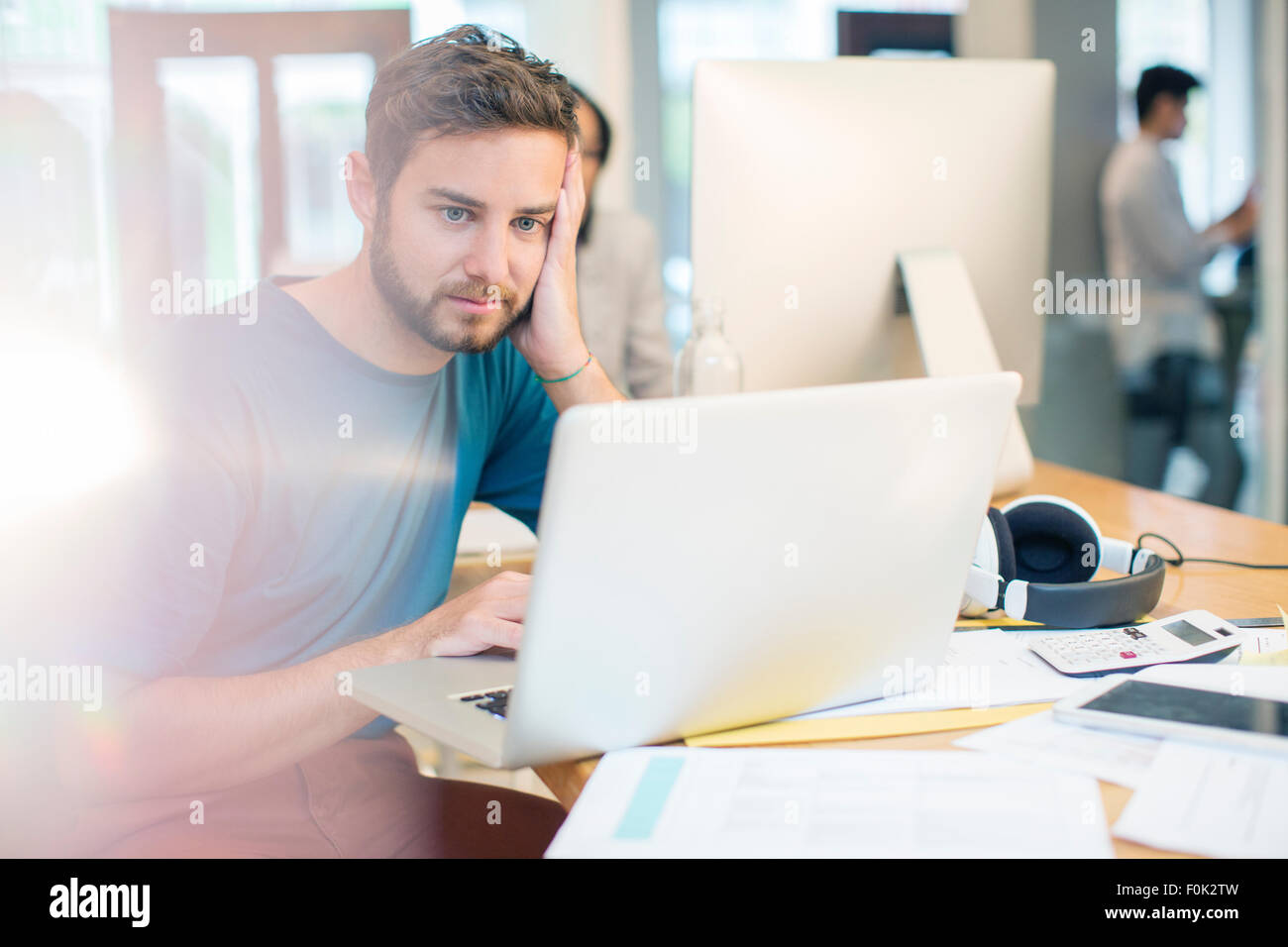 Grave imprenditore creativo utilizzando laptop con testa in mani in ufficio Foto Stock