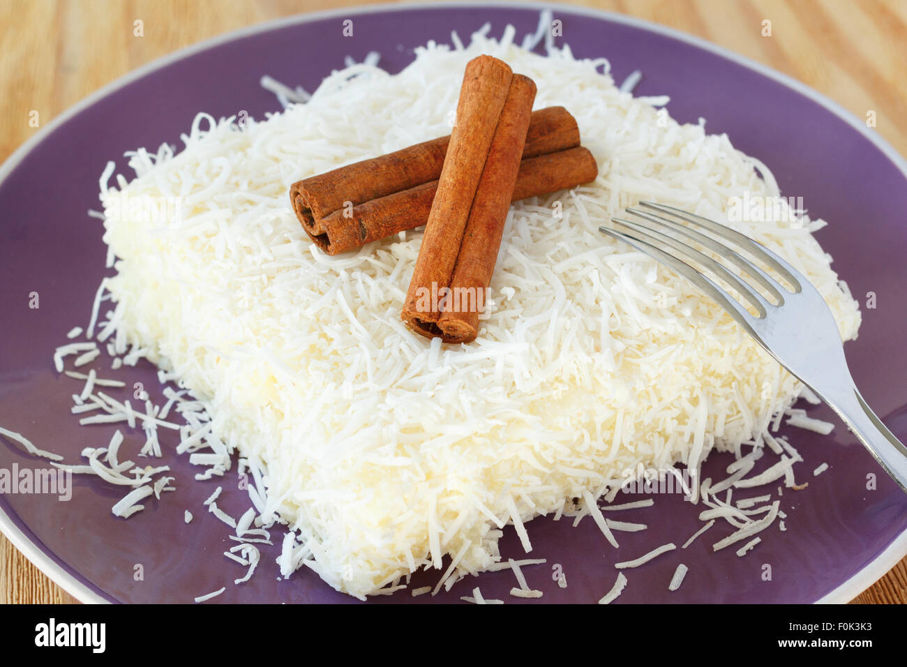 Brasiliano dessert tradizionale: dolce (cuscus tapioca) pudding (cuscuz doce) con noce di cocco sulla piastra viola sul tavolo di legno. Sele Foto Stock