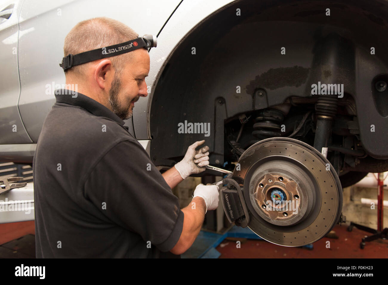 Un meccanico di automobili si inserisce nuove pastiglie dei freni di un auto in un garage auto durante un MOT. Foto Stock