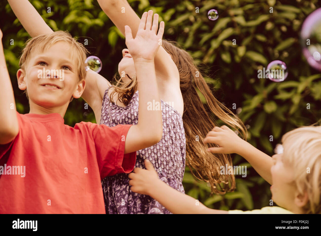 Tre bambini che giocano con il soffiare bolle di sapone in giardino Foto Stock