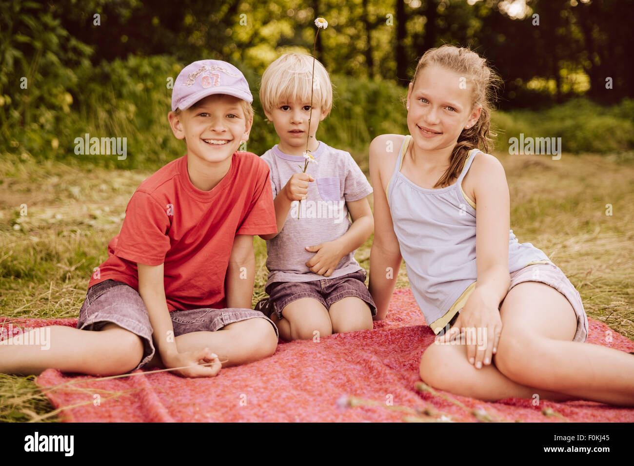 Tre bambini seduti su una coperta sul prato Foto Stock