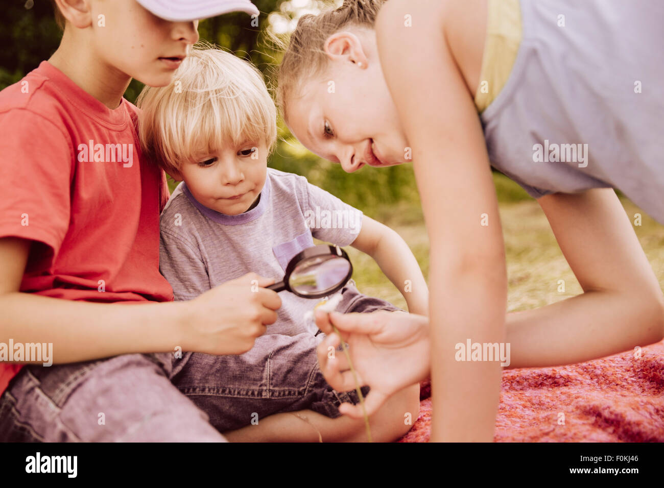 Tre bambini su una coperta di guardare attraverso una lente di ingrandimento Foto Stock